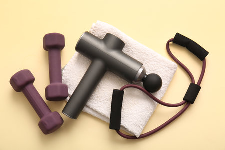 Percussive massager, clean towel, expander and dumbbells on color backgroundの写真素材