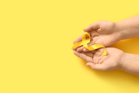 Female hands with yellow ribbon on color background. Sarcoma concept.の写真素材