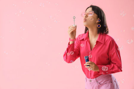 Happy young woman blowing soap bubbles on pink background