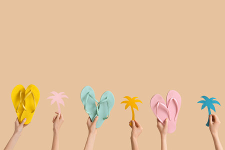 Hands holding three pairs of flip flops with paper palms on beige backgroundの写真素材