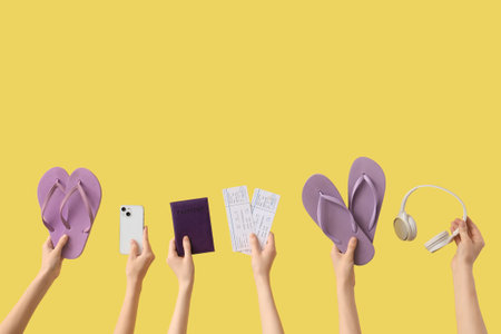 Hands holding two pairs of flip flops with mobile phone, headphones and passport with tickets on yellow backgroundの写真素材