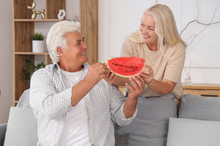 Mature couple with slice of watermelon at homeの写真素材