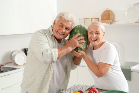Mature couple checking watermelon for ripeness in kitchenの写真素材