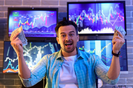 Happy male trader with dollar banknotes in office at night