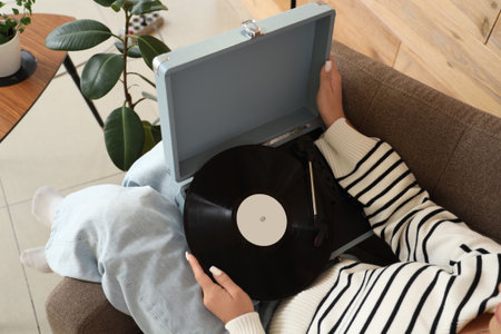 Young woman with record player in armchair at home, closeupの写真素材
