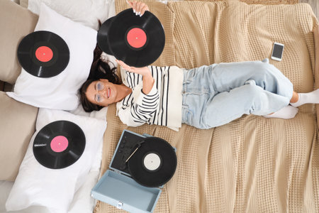 Beautiful woman with vinyl disks for record player lying on bed, top viewの写真素材