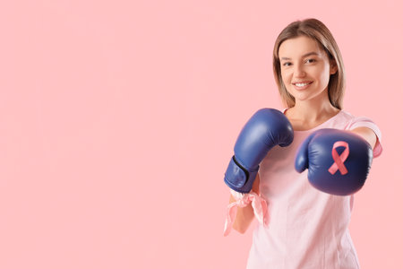 Young woman in boxing gloves with pink ribbon on color background. Breast cancer awareness conceptの写真素材