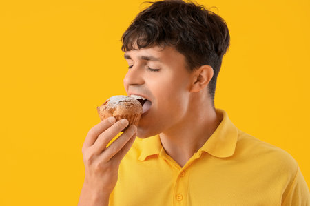 Young man eating tasty muffin on yellow background, closeupの写真素材