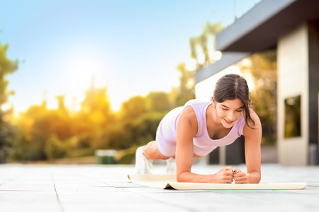 Sporty young woman doing plank on fitness mat outdoors