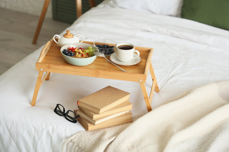Tray with breakfast, books and eyeglasses on bed in roomの写真素材