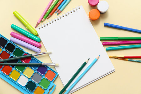 Composition with blank notebook, paints, pencils and markers on color background