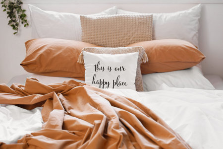 Big comfortable bed with crumpled linen and pillow with text THIS IS OUR HAPPY PLACE in room....