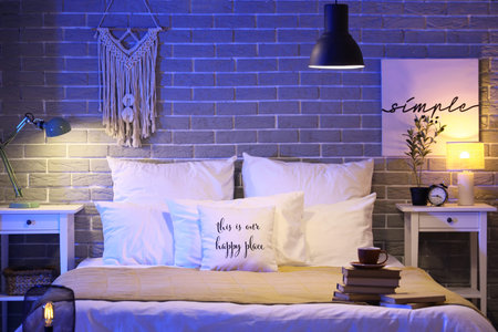 Interior of dark bedroom with glowing lamps, coffee cup and books on bed at night