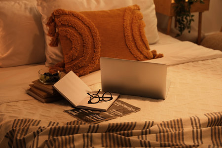 Laptop with books, eyeglasses and fruits on bed in eveningの写真素材