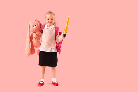 Cute little schoolgirl with big pencil and plush toy on pink background