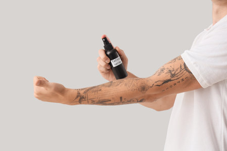 Young man spraying his tattooed arm on light background, closeupの写真素材