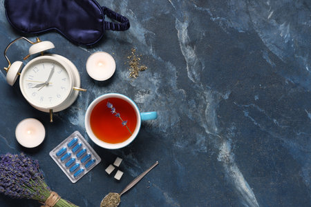 Cup of tea with sleep mask, alarm clock, pills, lavender flowers and burning candles on blue backgroundの写真素材