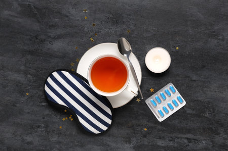 Cup of tea with sleep mask, pills and burning candle on black backgroundの写真素材