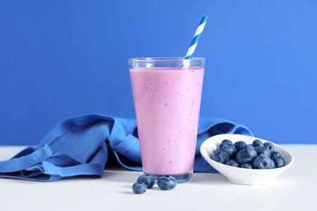 Glass of fresh smoothie and bowl with blueberries on colorful backgroundの写真素材