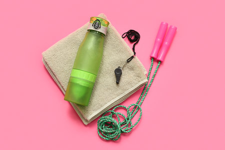 Towel, whistle, sports water bottle and jumping rope on pink backgroundの写真素材