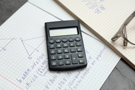 Copybooks with math formulas and calculator on table, closeup