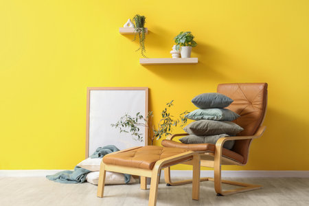 Brown armchair with footrest and stack of soft cushions near yellow wallの写真素材