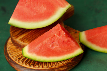 Wooden boards with pieces of sweet watermelon on green background