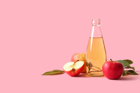 Bottle of fresh apple cider and fruits on pink background