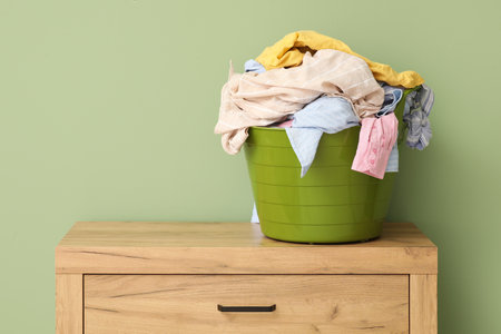 Basket with laundry on chest of drawers near green wallの写真素材