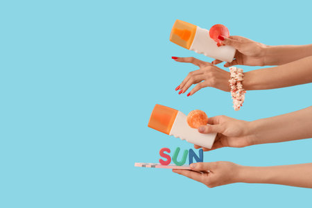 Female hands with bottles of sunscreen creams, shells and word SUN on blue background