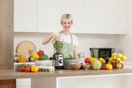 Young woman putting spinach into blender in kitchenの写真素材