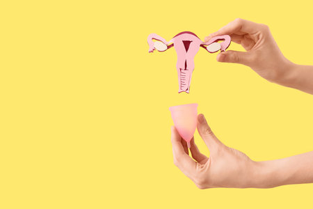 Woman with paper uterus and menstrual cup on yellow background