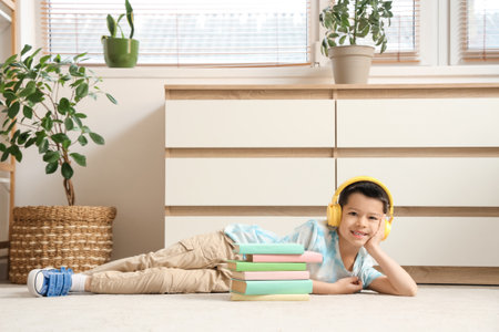 Cute little Asian boy in headphones listening to audiobook with books while lying on carpet in living roomの写真素材