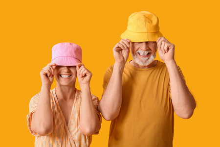 Mature couple in bucket hats on yellow backgroundの写真素材