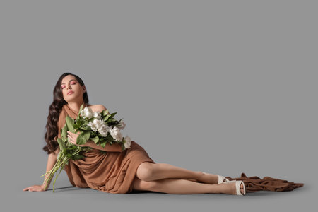 Beautiful young woman with bouquet of white peony flowers sitting on gray backgroundの写真素材