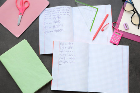 Copybooks with math formulas, book and different stationery on dark background