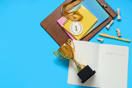 Notebook with text GOALS 2025, gold cup, medal and chess pieces on blue background