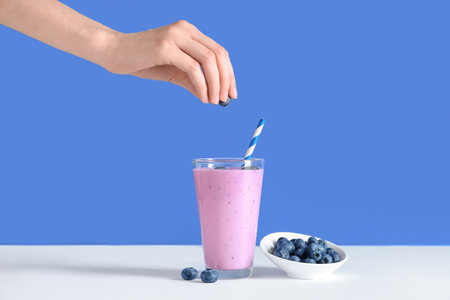Female hand with glass of fresh smoothie and bowl of blueberries on colorful backgroundの写真素材
