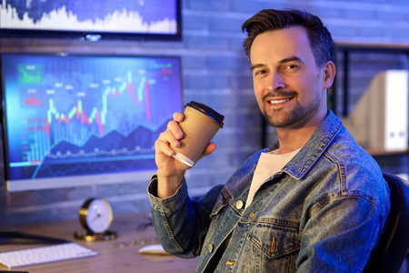 Male trader with cup of coffee in office at night, closeup