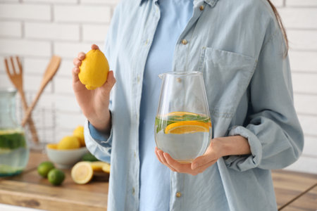 Young woman holding jug of lemon infused water with mint in kitchenの写真素材