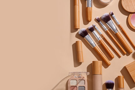 Stylish makeup brushes with cosmetic products on beige backgroundの写真素材