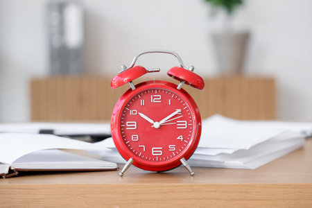 Red alarm clock on desk in office, closeup