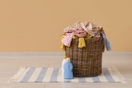 Wicker basket with laundry on floor with washing gel near beige wall