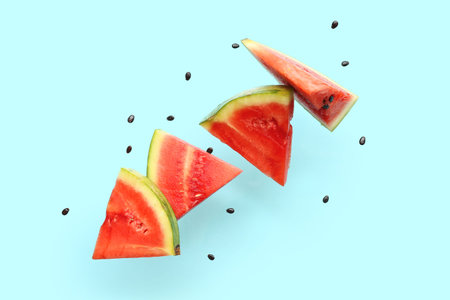 Flying pieces of fresh watermelon and seeds on blue background
