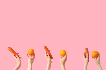 Hands with fresh oranges and carrots on pink backgroundの写真素材