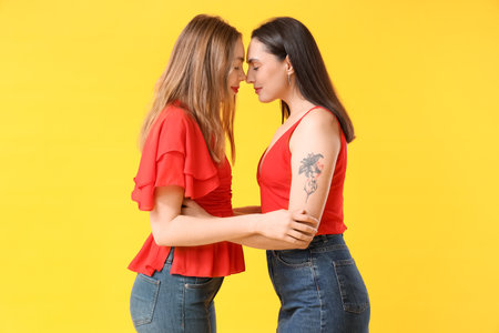 Beautiful young lesbian couple on yellow backgroundの写真素材