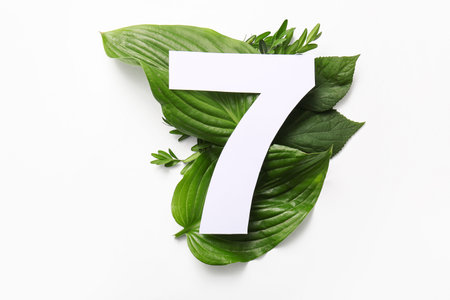 Green leaves with paper number seven on white background. Top view