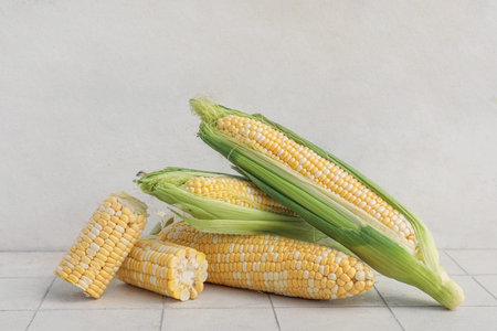 Fresh corn cobs on white tile table