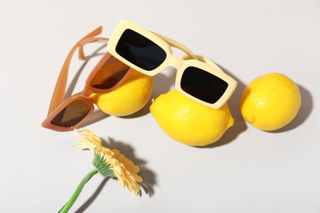 Stylish sunglasses with fresh lemons and gerbera flower on gray backgroundの写真素材