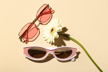 Stylish sunglasses and gerbera flower on beige backgroundの写真素材